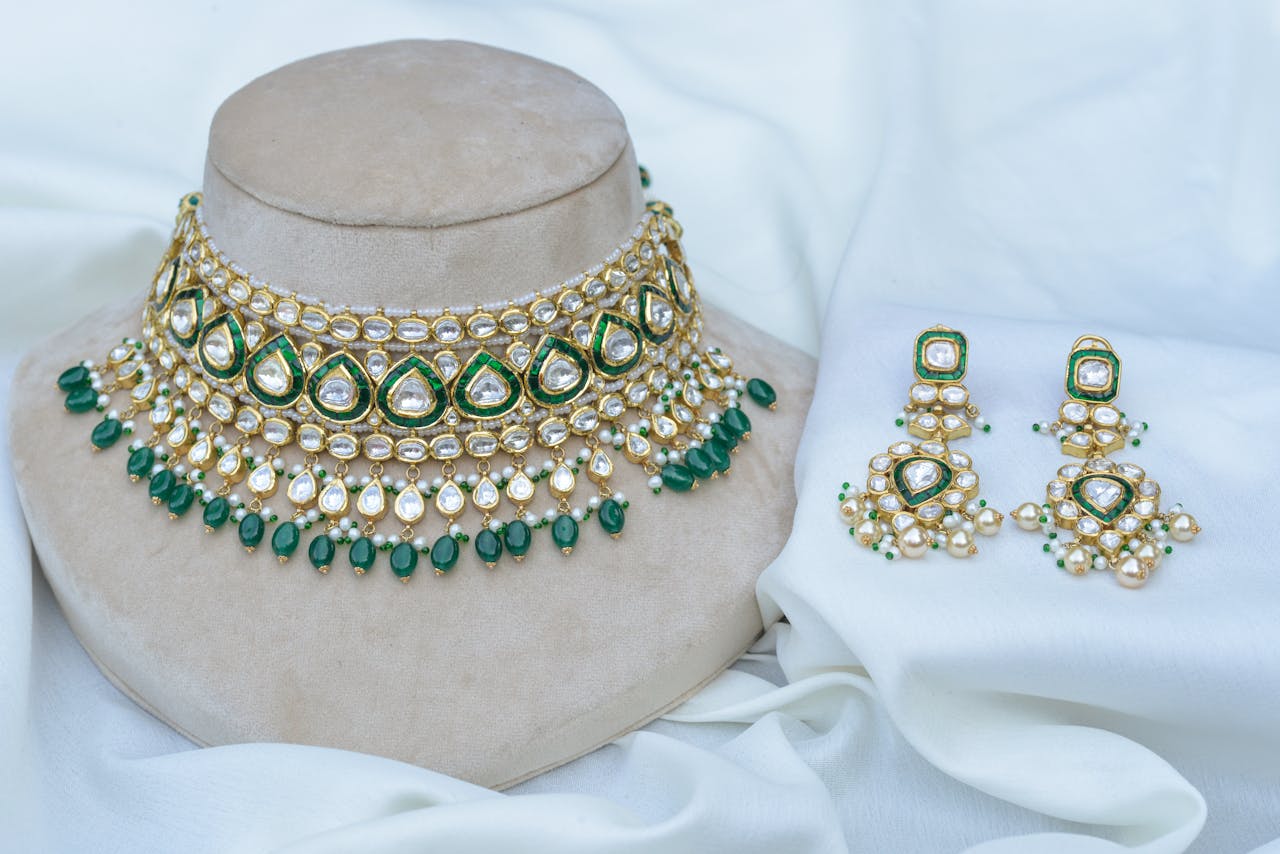 gallery-05 Luxurious gold and green jewelry set featuring intricate beadwork and pearls displayed on a fabric backdrop.